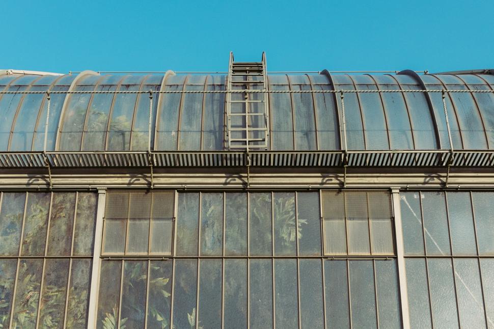 Free Image of Ladder on glass building under bright blue sky view 