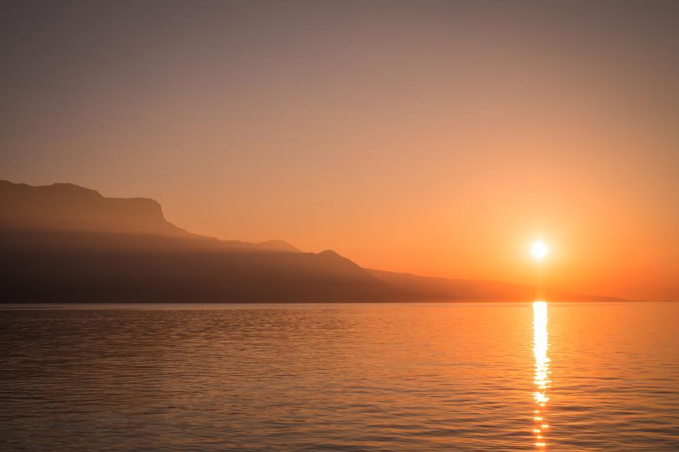 Free Image of Sunset over calm water with mountain silhouette 
