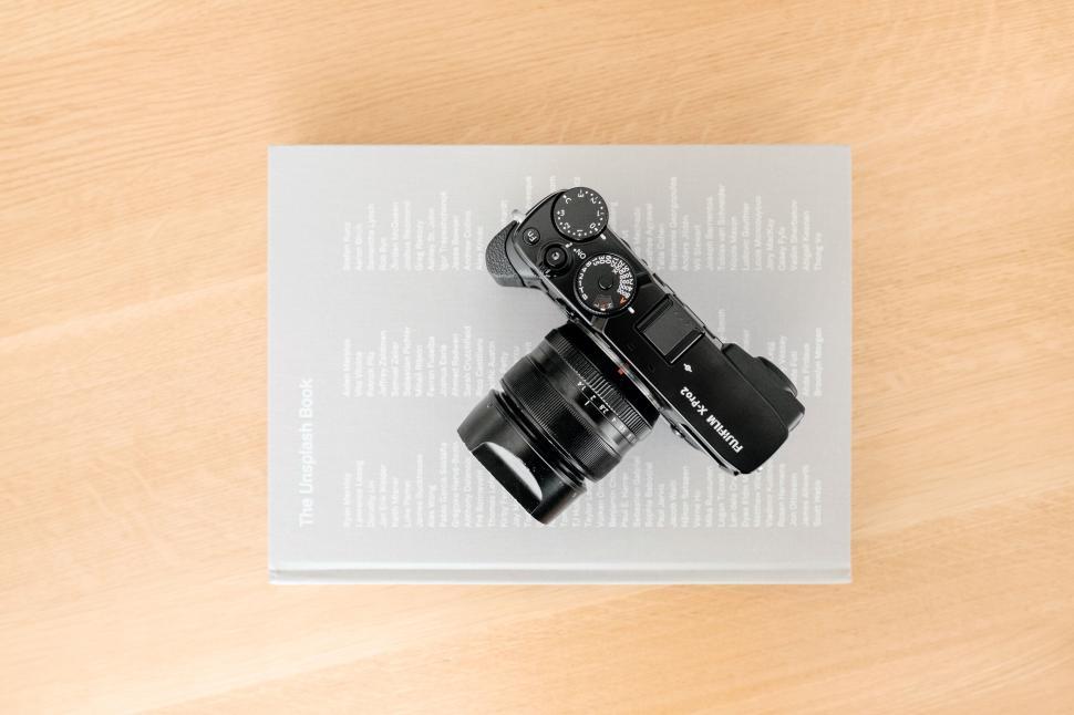Free Image of Modern camera placed on a grey book on a wooden table 