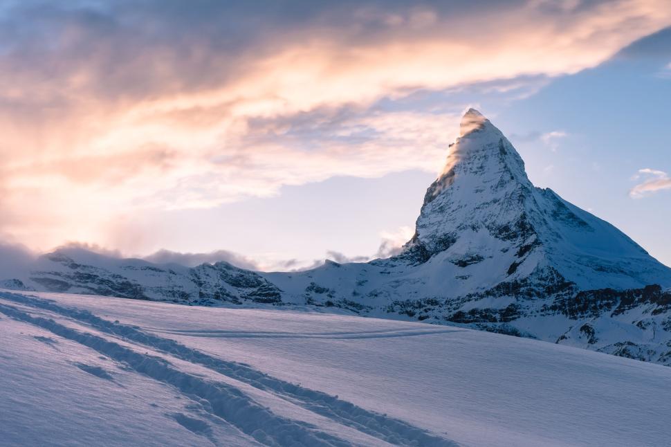 Free Image of Snow-covered mountain peak under a dramatic cloudy sky 