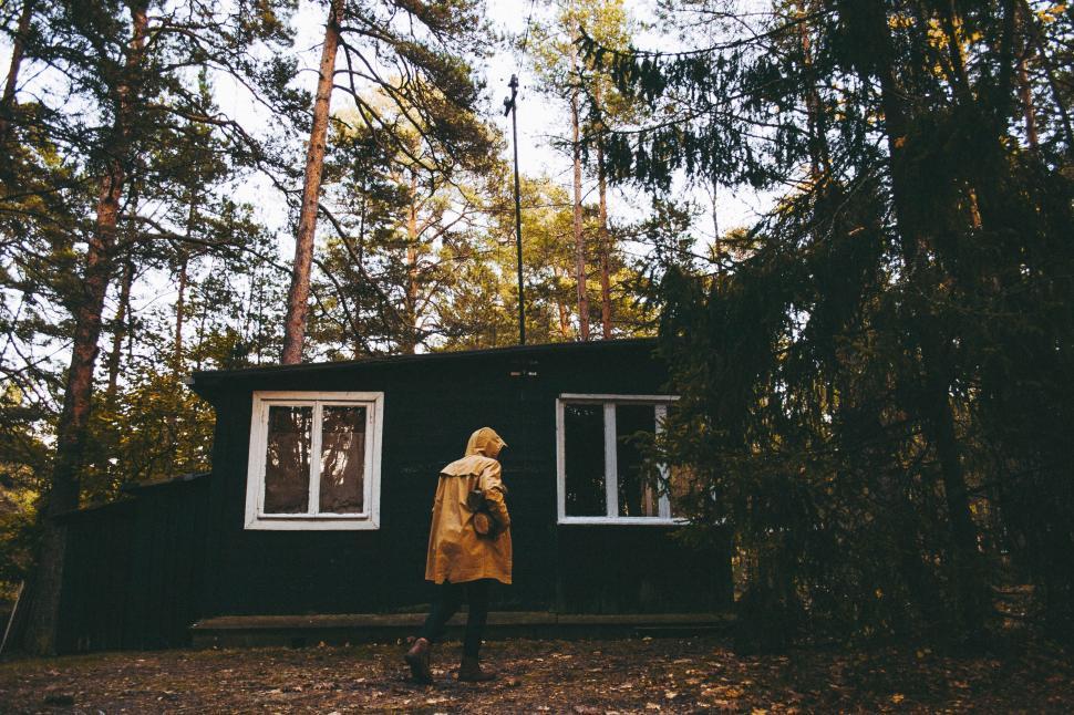 Free Image of Person outside dark cabin in forest wearing a yellow coat 