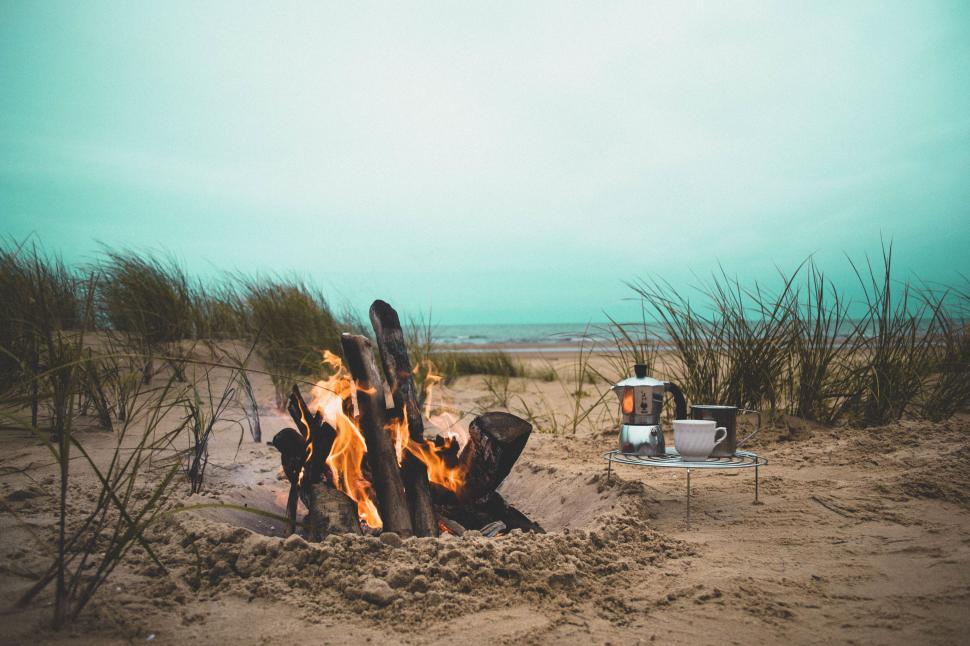 Free Image of Cozy beach campfire with coffee setup by the sea 