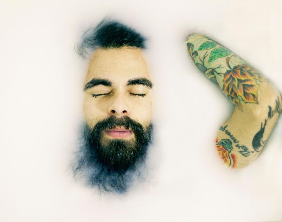 Free Image of Man with beard and tattooed arm in milk bath relaxing. 
