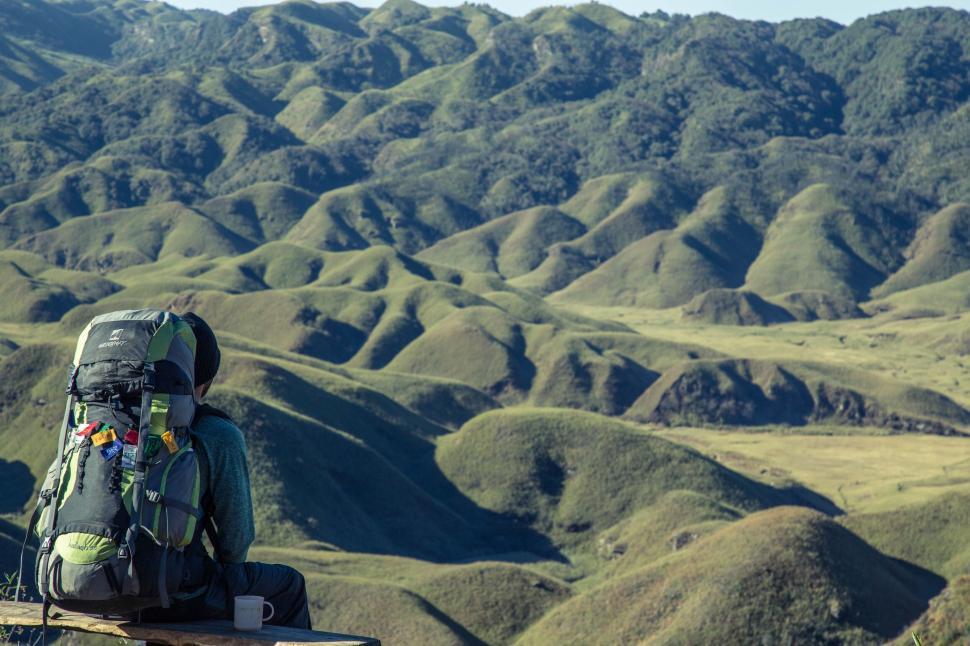 Free Image of Hiker admiring the vast, lush green hills and peaks 