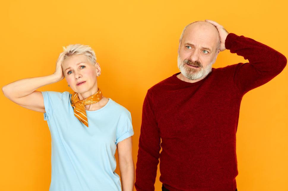Free Image of Attractive emotional mature female and her gray haired husband having memory loss problem posing isolated with forgetful facial expression, holding hands on heads, being puzzled and confused 