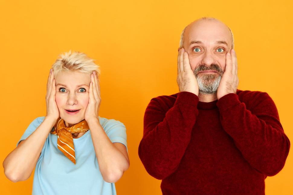 Free Image of Shock, astonishment and surprise concept. Funny European bearded senior male and blonde female being shocked with amazing unexpected news, holding hands on cheeks, keeping mouth wide opened 