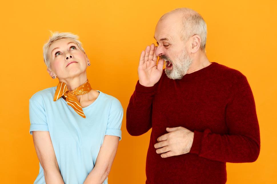 Free Image of Angry emotional elderly male in casual clothes holding hand at face, opening mouth widely and shouting at his careless wife who is looking upwards, as if not hearing him, paying no attention 