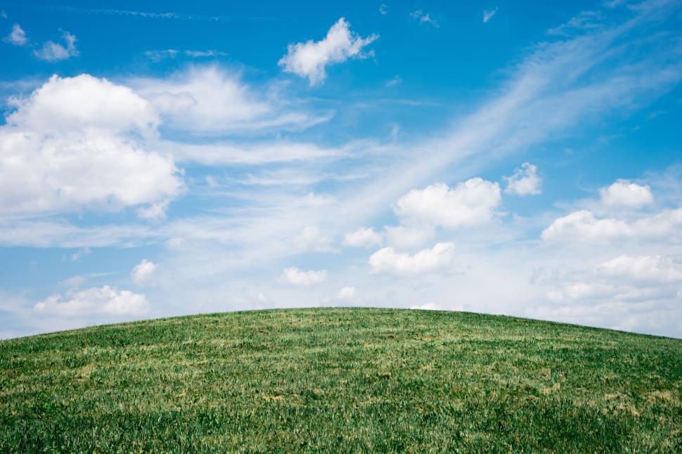 Free Image of Grassy hill under a blue sky with soft white clouds 