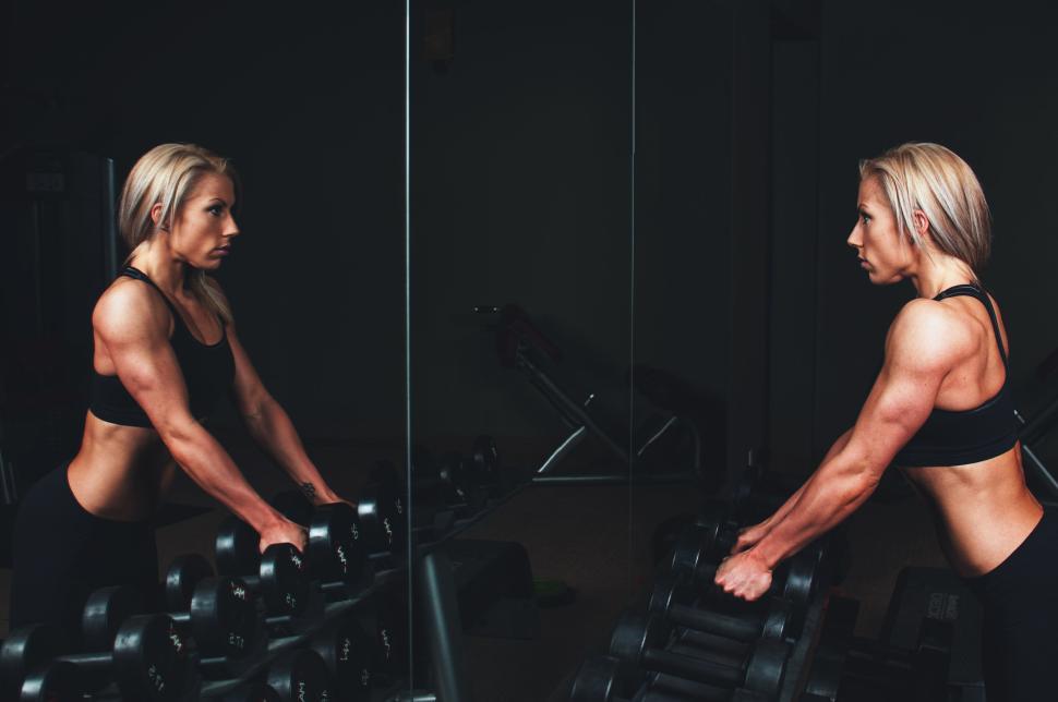 Free Image of Woman weightlifting in front of mirror in dimly lit gym 