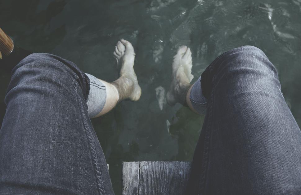 Free Image of Person dipping feet in calm water from wooden deck 