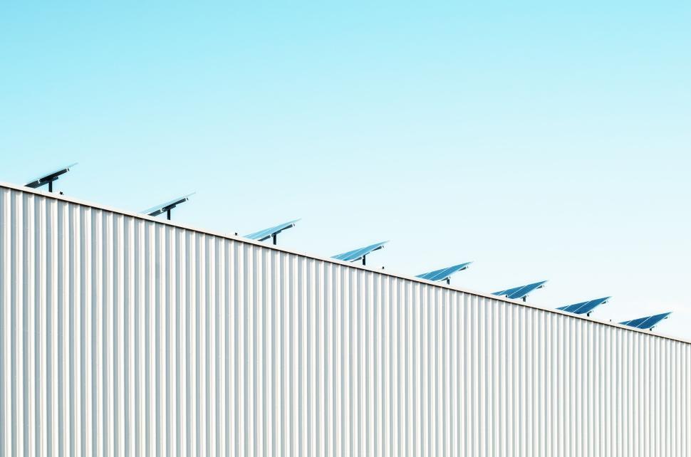 Free Image of Solar panels line the edge of a corrugated building roof 