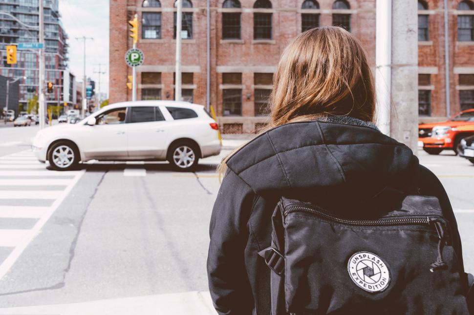 Free Image of Person with backpack stands at city street crosswalk 