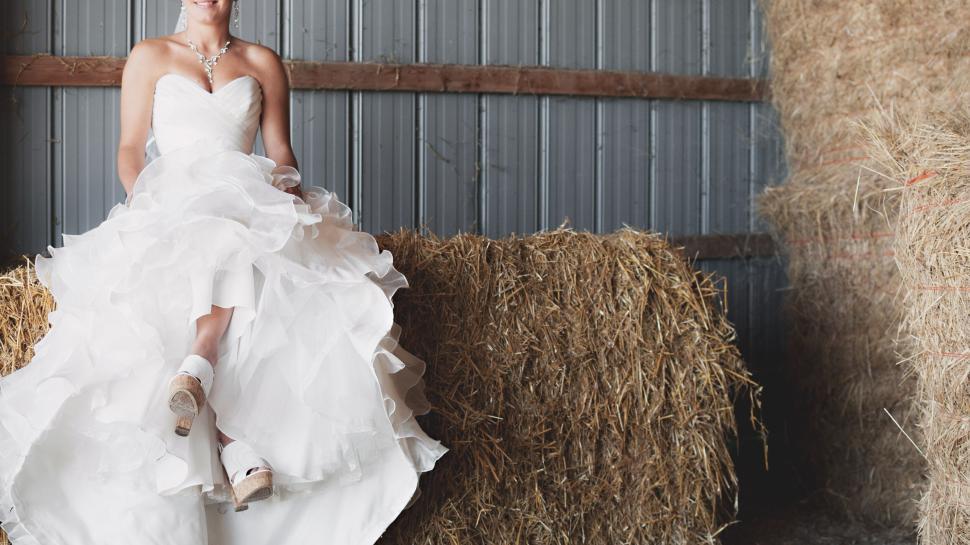 Free Image of Bride in wedding dress sitting on hay bales in barn 
