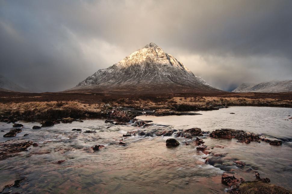 Free Image of Peaked mountain glowing under a dramatic sky by river 