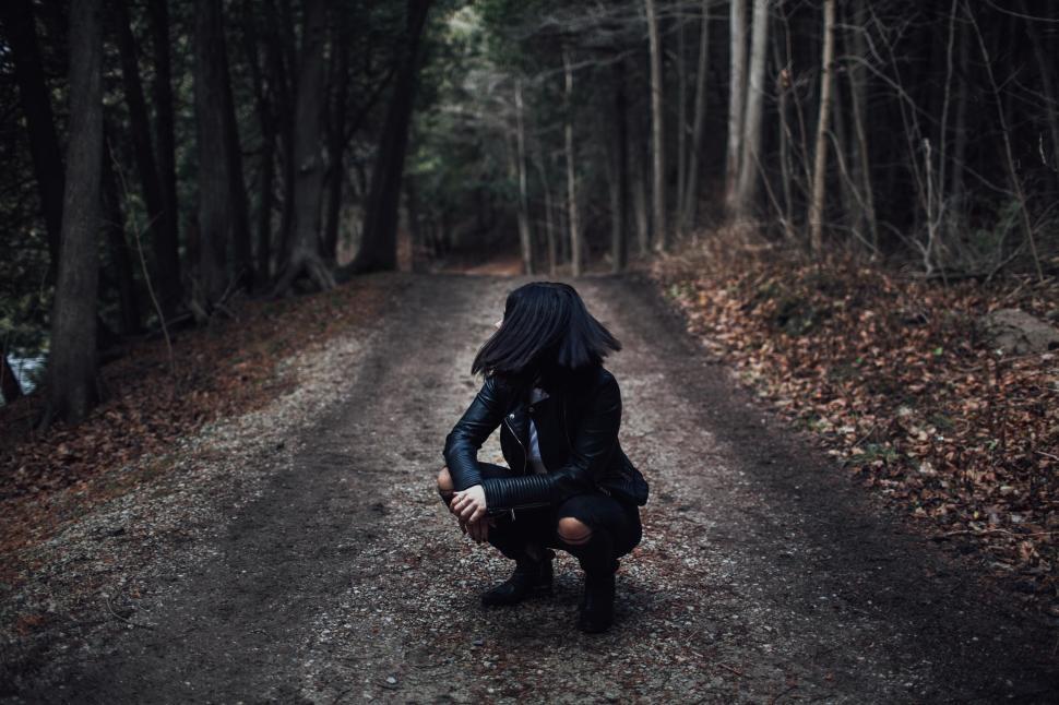 Free Image of Woman in dark clothes crouches on forest path 
