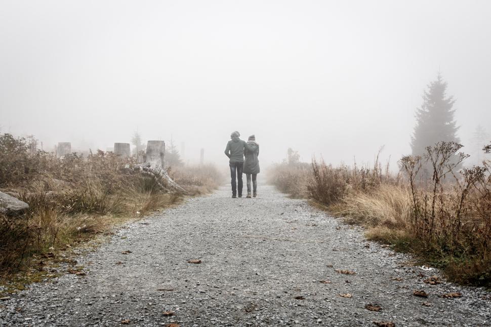 Free Image of Two people walking on foggy trail amidst dry foliage around. 