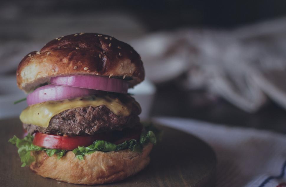 Free Image of Juicy cheeseburger with toppings on a round wooden plate 