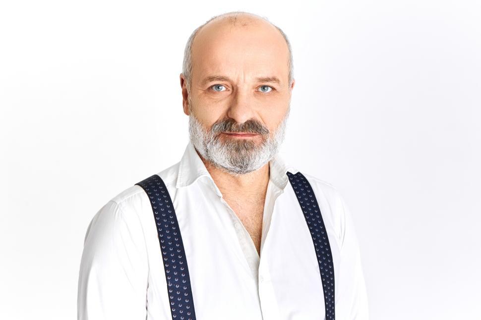 Free Image of People, age, maturity, style and elegance concept. Isolated image of attractive fashionable senior man with thick gray beard looking at camera with confident smile, wearing white shirt and braces 