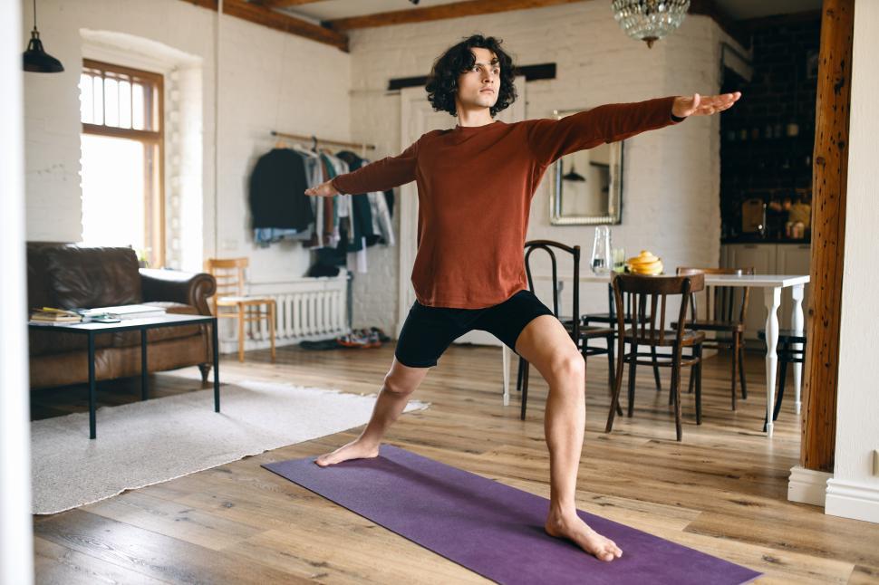 Free Image of Full length image of handsome young male with strong athletic body practicing yoga indoors, standing in warrior 2 pose or virabhadrasana, taking deep breaths. Sports, active lifestyle and vitality 