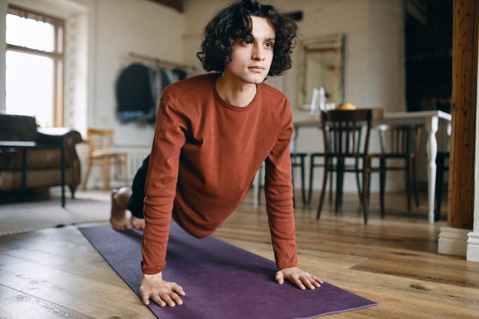 Free Image of Self determined confident young man with curly hair doing plank on fitness mat during morning training at home because of social distancing. Endurance, strength, energy and weight loss concept 