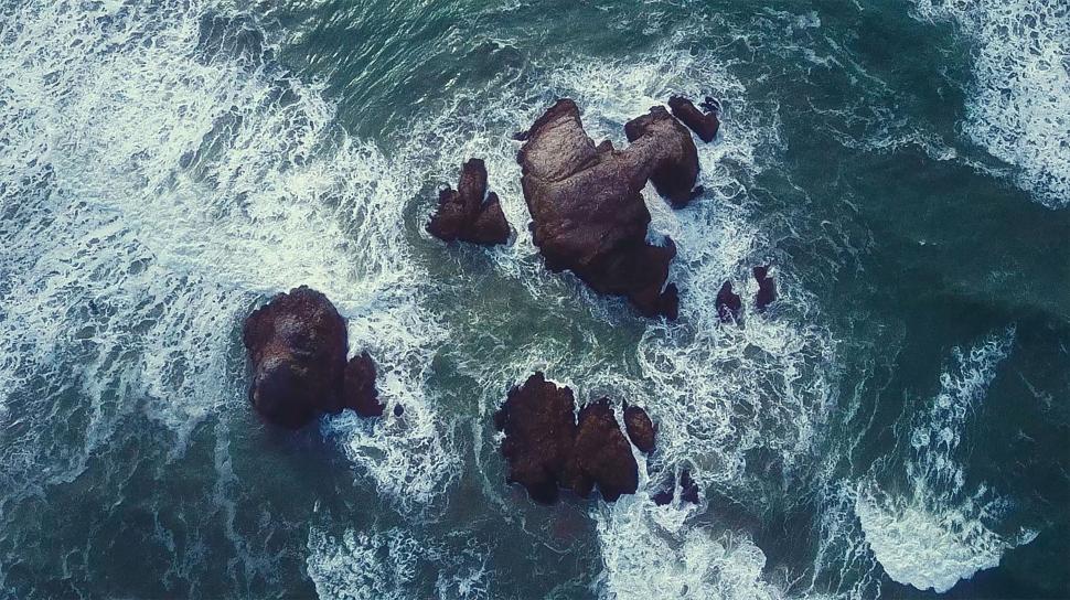 Free Image of Aerial view of ocean waves crashing on rocky shore. 