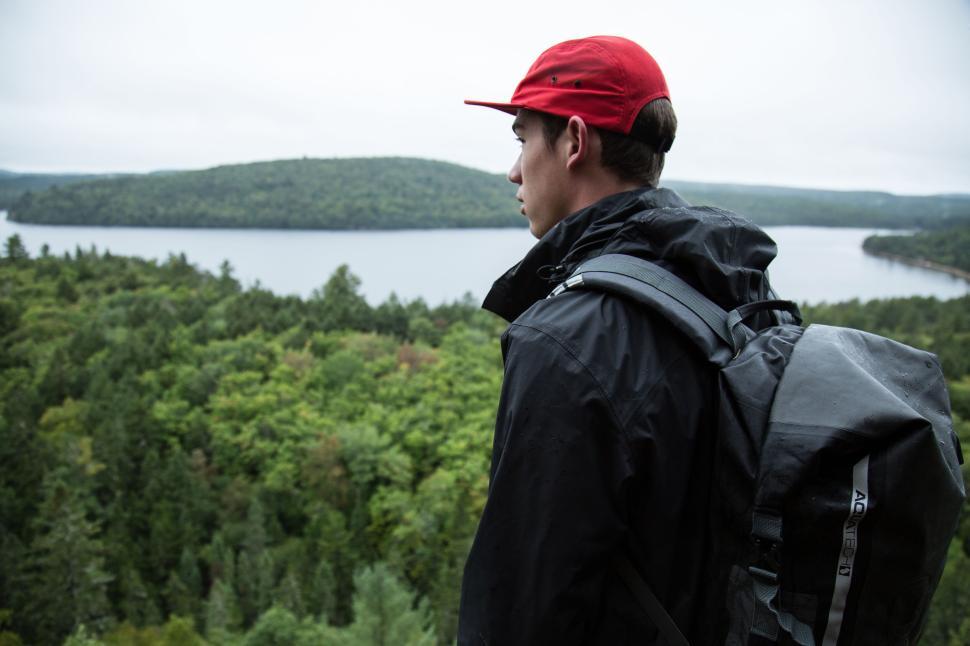 Free Image of Person with red hat overlooking vast forest and lake. 