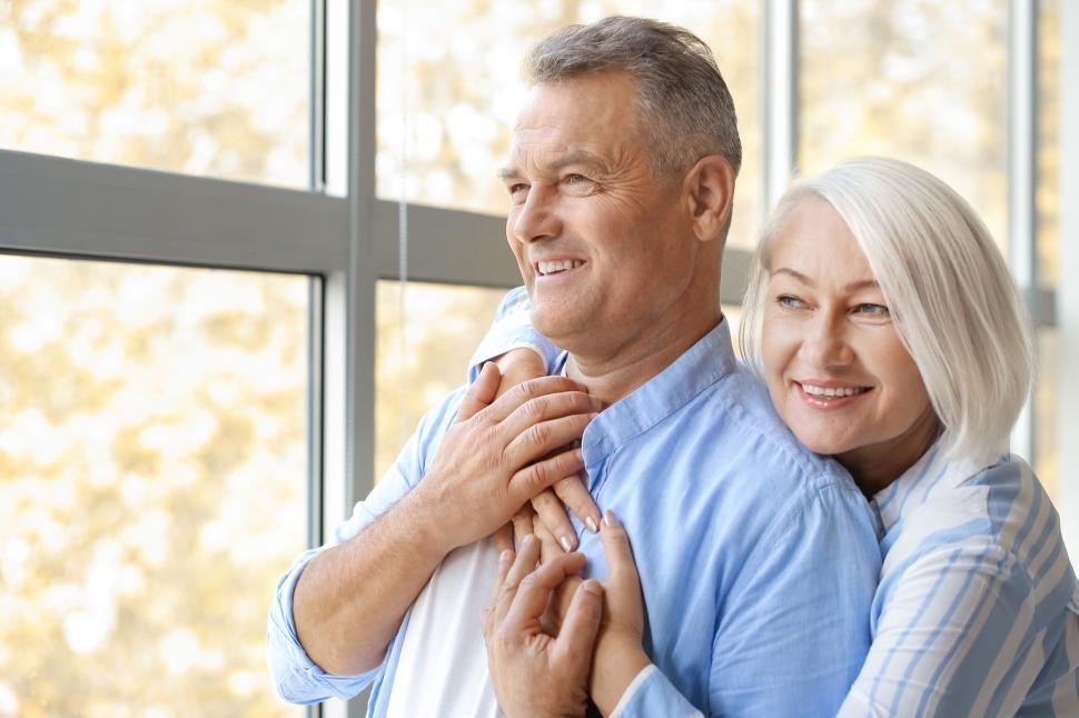 Free Image of Senior couple smiling and posing near a bright window 