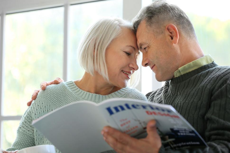 Free Image of Couple Reading a Magazine Together by the Window Light 