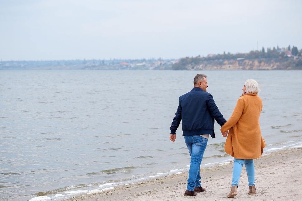 Free Image of Couple holding hands while walking on the beach 