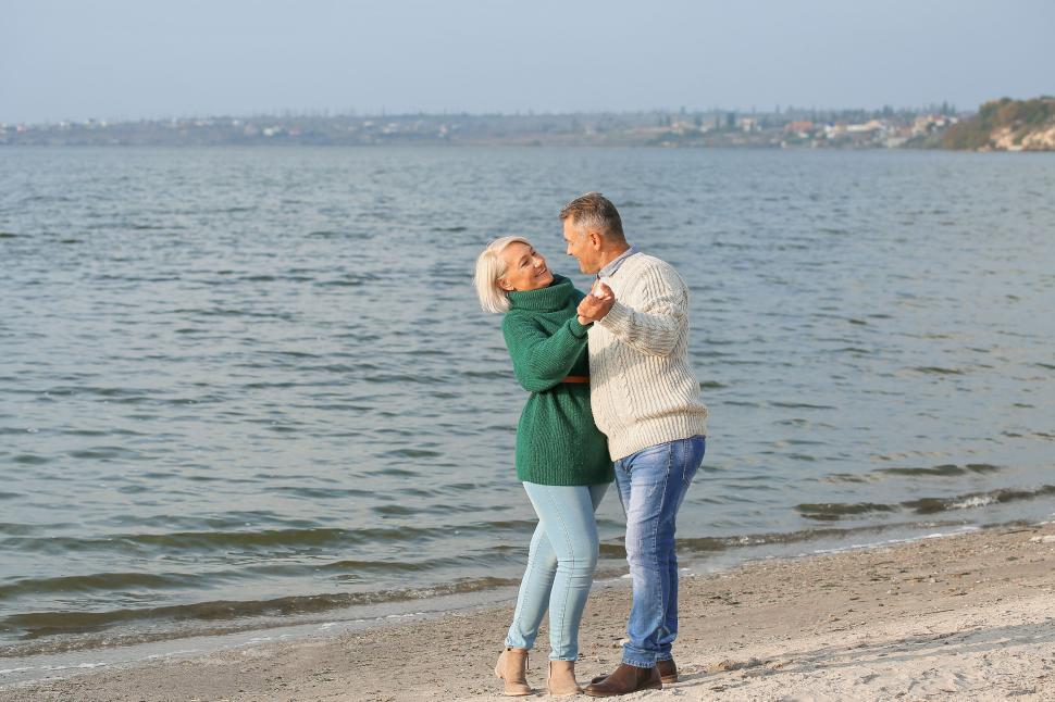 Free Image of Couple dancing on a sandy beach by the calm water 