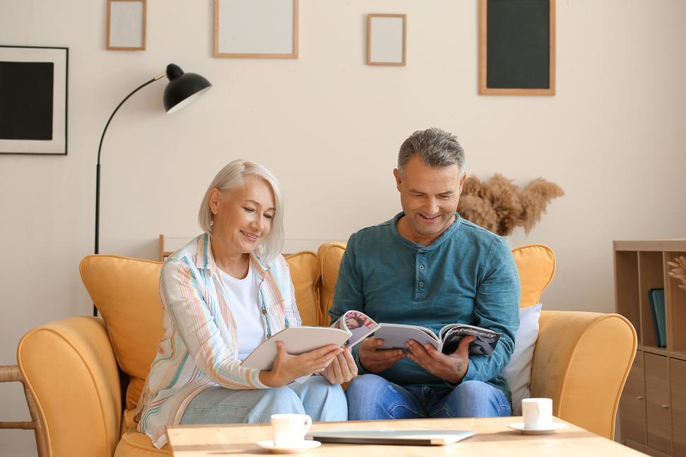 Free Image of Senior couple reading magazines on yellow couch. 