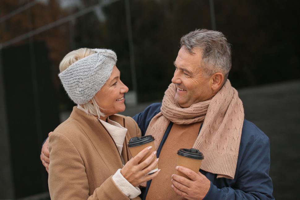 Free Image of Couple sharing warm drinks with smiles outdoors. 