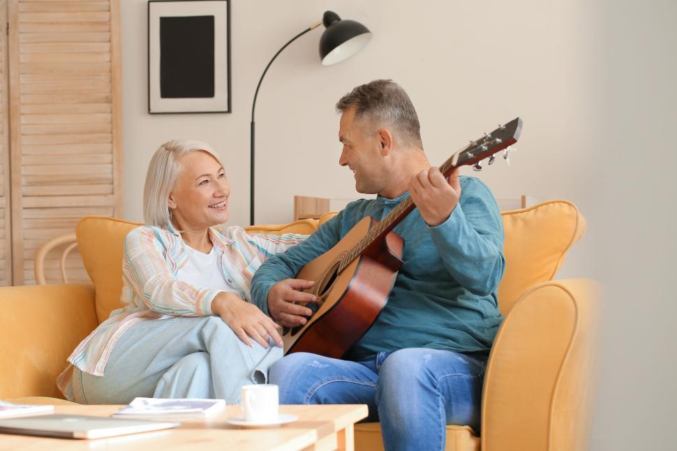 Free Image of Man serenading woman with guitar on a comfy sofa 