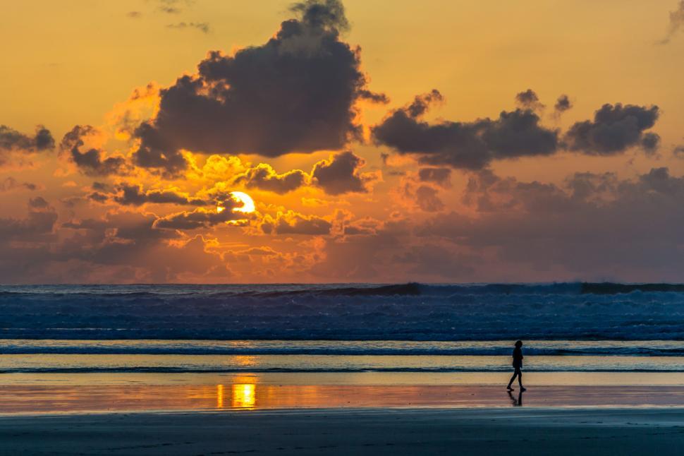 Free Image of A solitary figure walking on the beach at sunset 