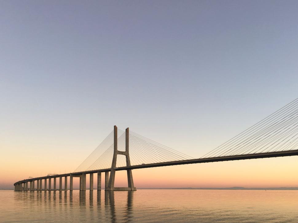 Free Image of Sunset over a long suspension bridge across calm water 