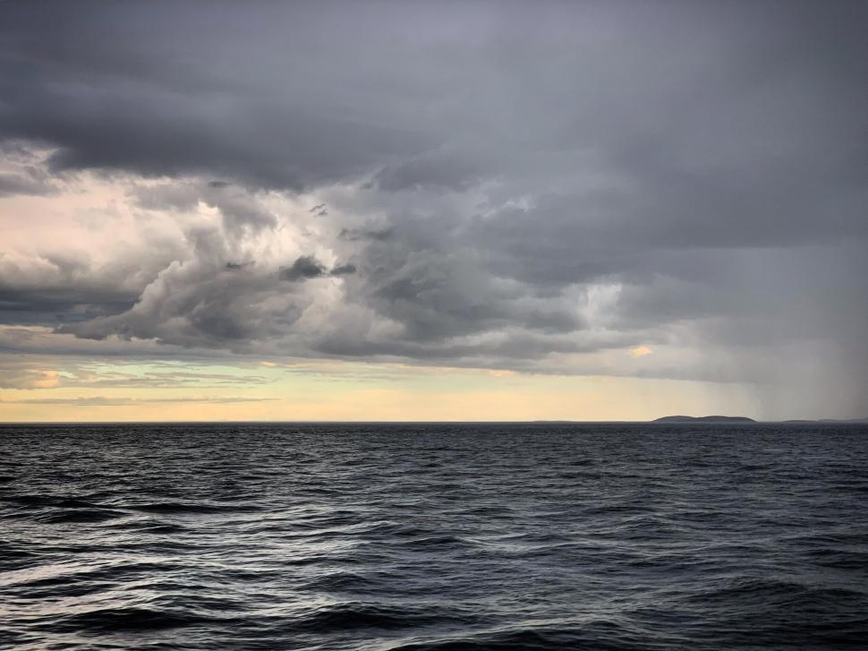 Free Image of A stormy sea under dark clouds with a distant island 
