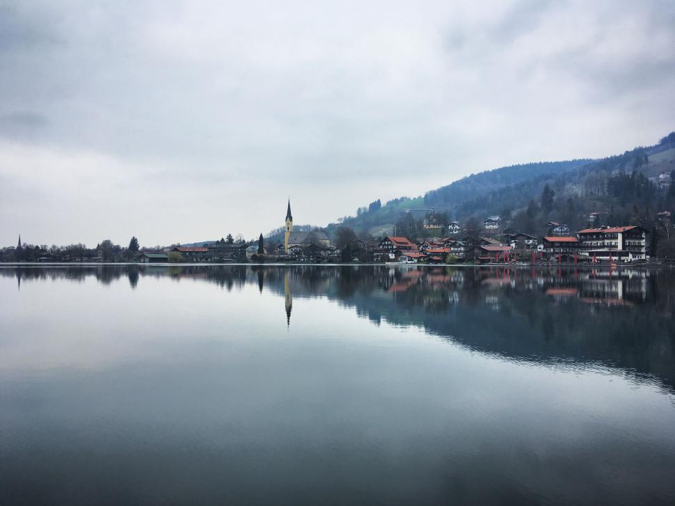 Free Image of Quiet town beside a calm reflective lake under grey skies 