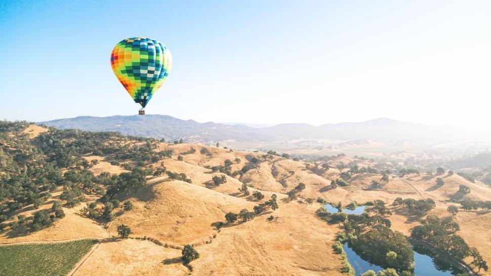 Free Image of Vibrant hot air balloon floating over rolling hills 