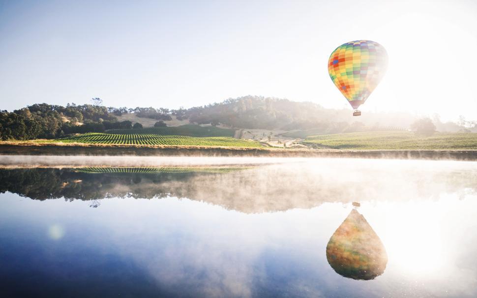 Free Image of Hot air balloon over serene lake reflecting the dawn light 