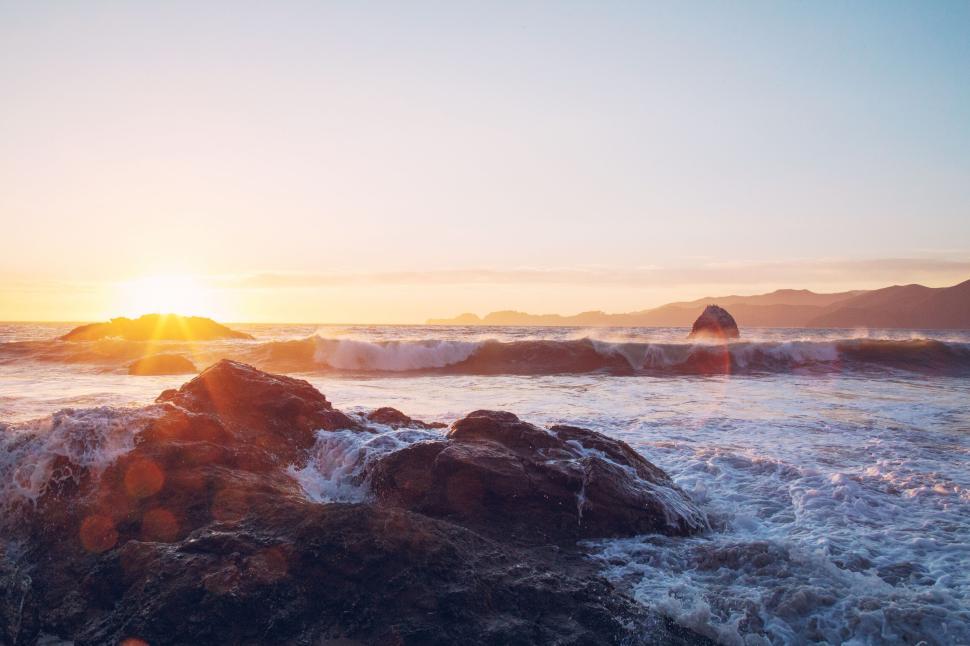 Free Image of Sunset over ocean waves with rocky shore view. 