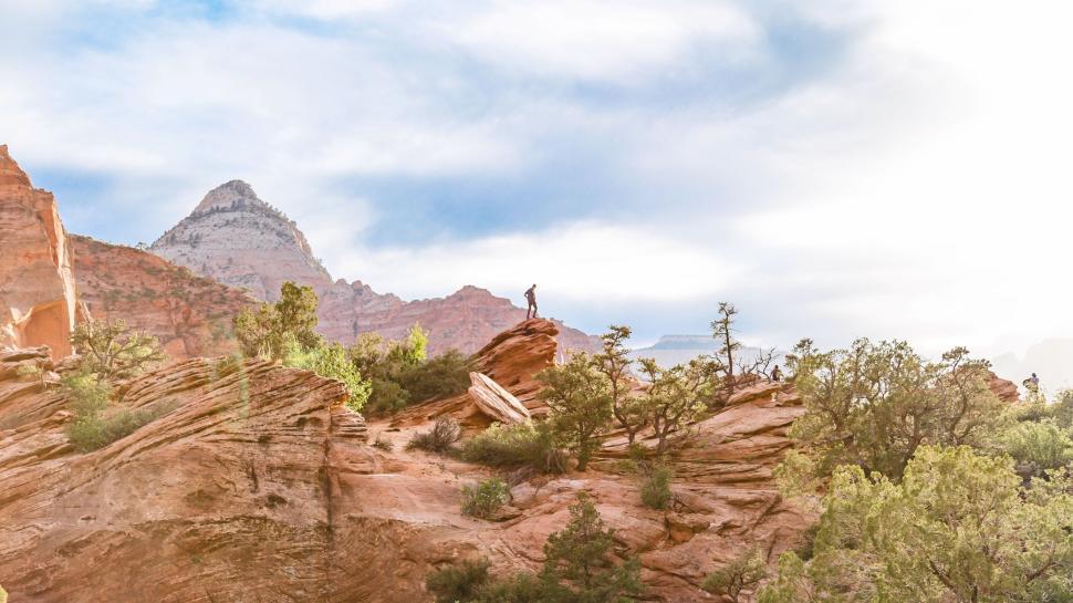 Free Image of Person stands on red rock formation with mountains behind. 
