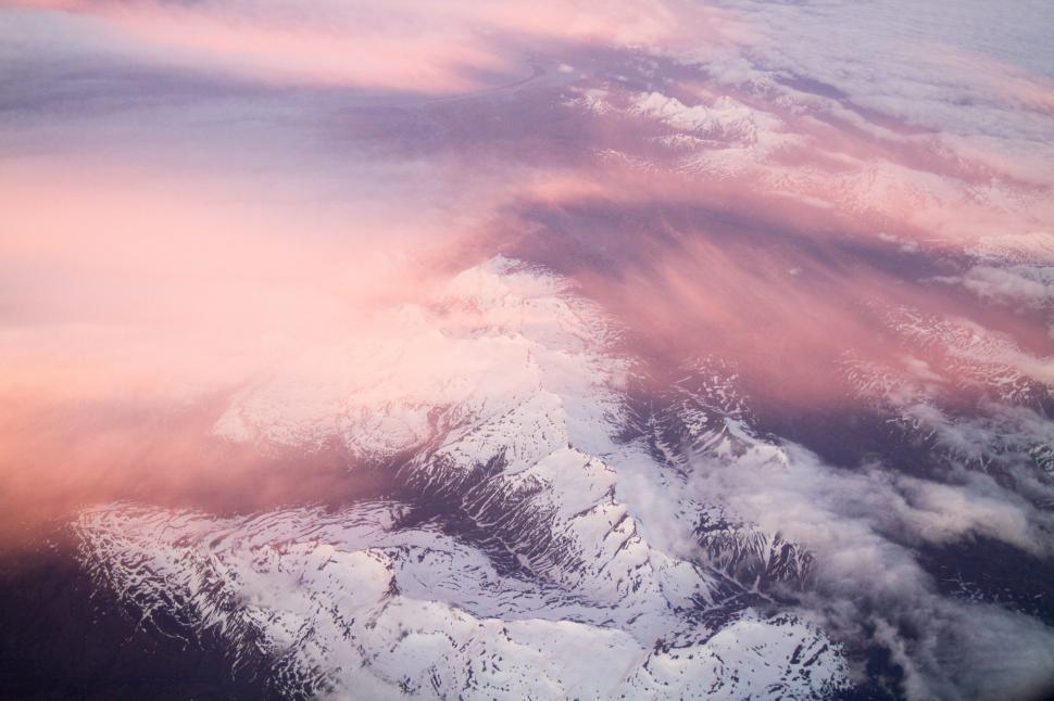 Free Image of Pink-tinted clouds over snowy mountains at sunrise. 