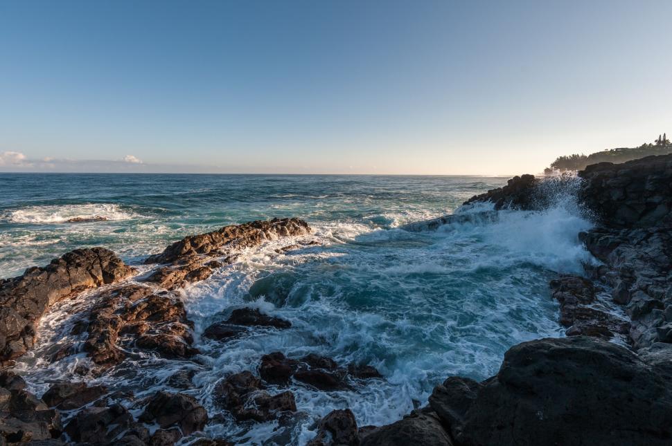 Free Image of Waves crash on rocky shoreline with blue skies overhead 