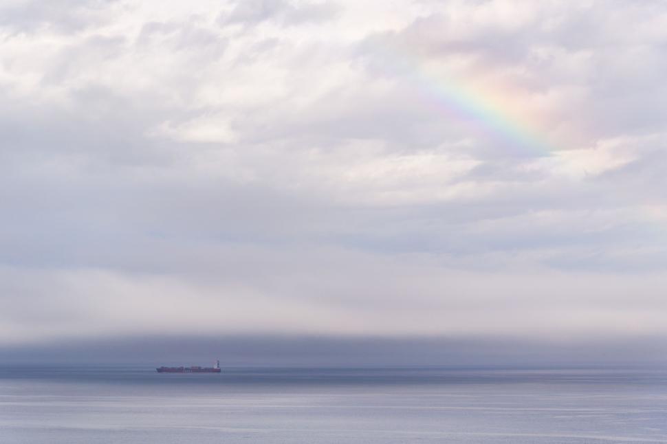 Free Image of A solitary rainbow over a calm sea with distant ship 