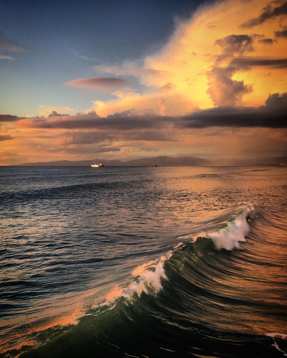 Free Image of Golden sunset reflecting on the ocean with waves crashing. 