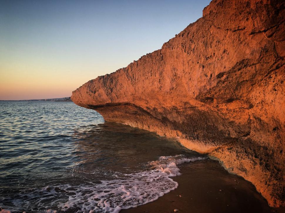 Free Image of Rocky cliff by the sea with sunset lighting 