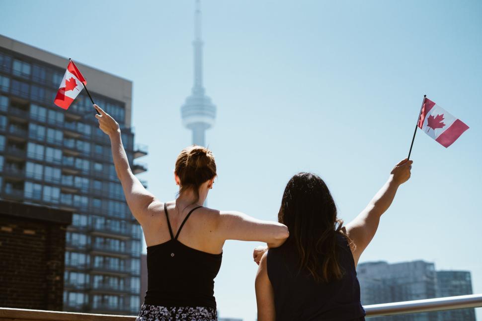 Free Image of Two people holding Canadian flags with CN Tower behind 