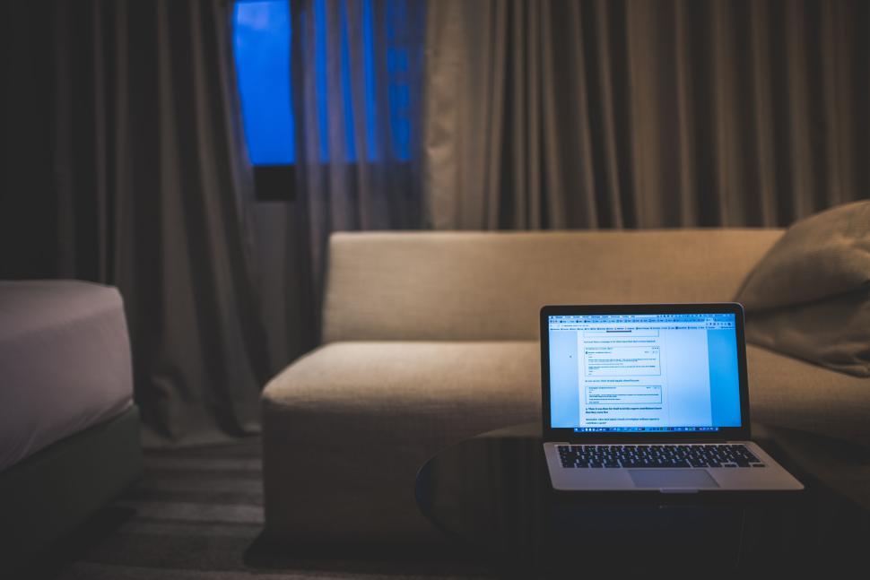 Free Image of Laptop on table with sofa in the background at dusk. 