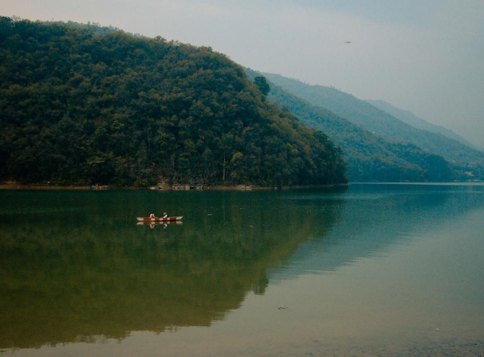 Free Image of Two people canoeing on a serene lake amidst green hills 