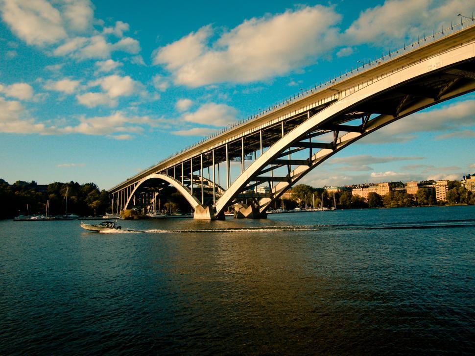 Free Image of Speedboat under a large arch bridge on a sunny day 